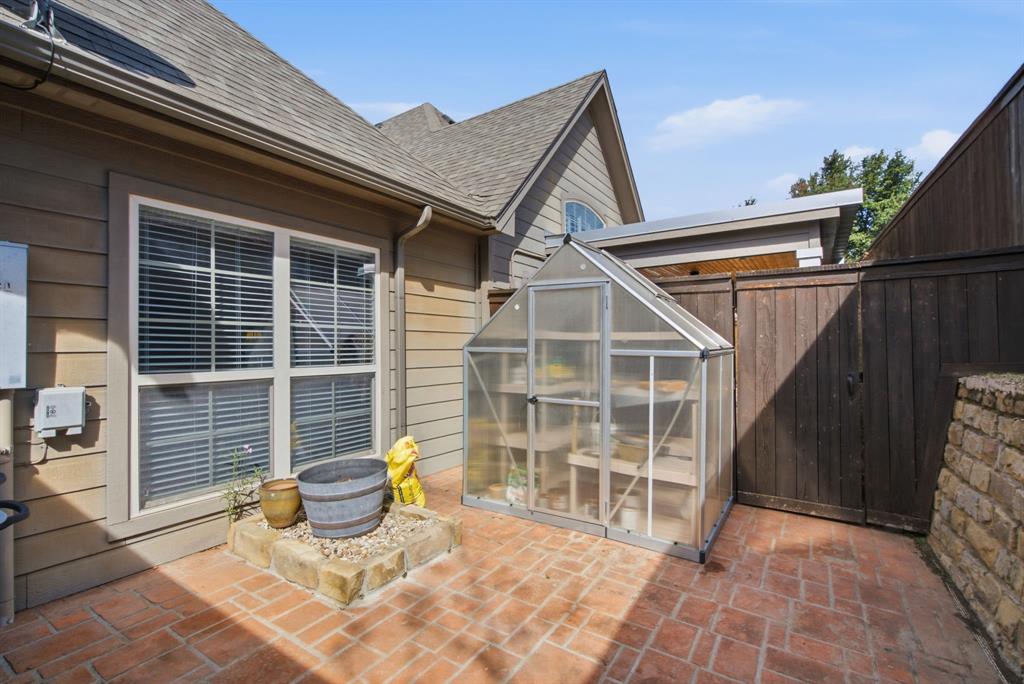 Side courtyard featuring brick paver flooring, a raised stone-walled planter, a freestanding greenhouse, and a perimeter privacy fence