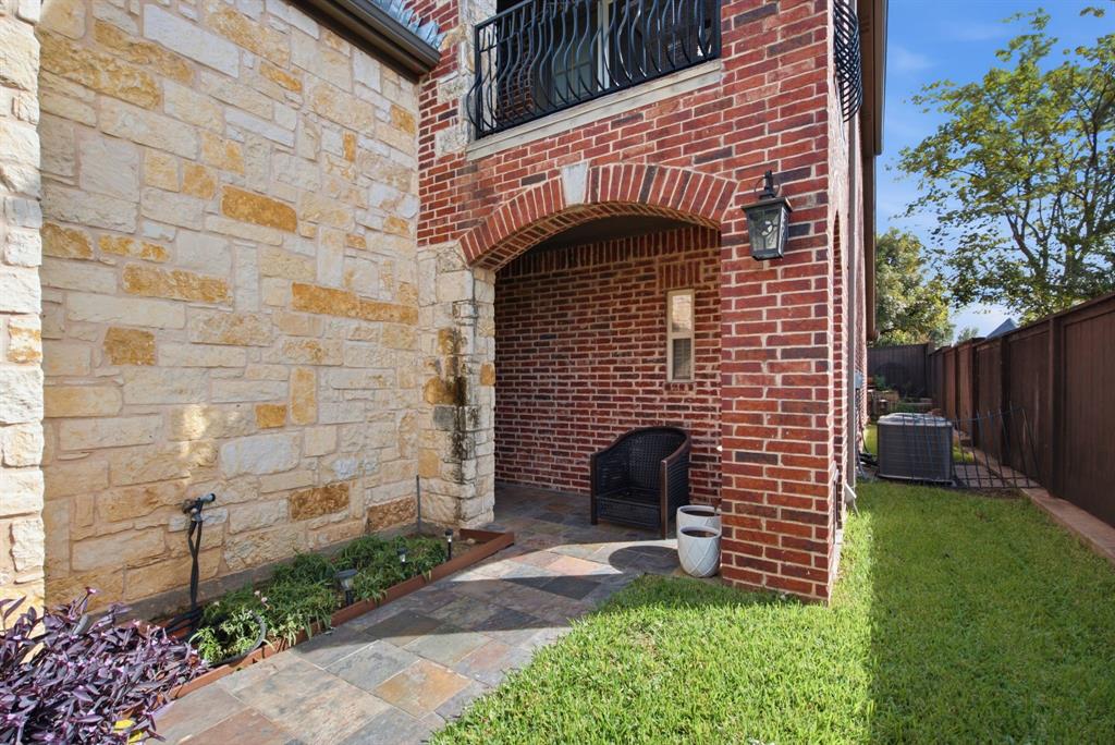 Exterior facade featuring masonry stone cladding and red brickwork, arched covered patio with stone tile flooring, and metal balcony railing