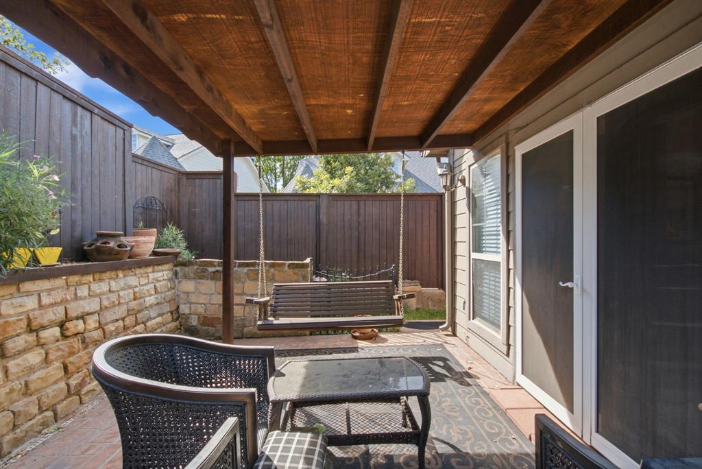 Covered back patio featuring a timber-frame pergola, natural stone retaining wall, paved flooring, and a swing set anchored to the structure