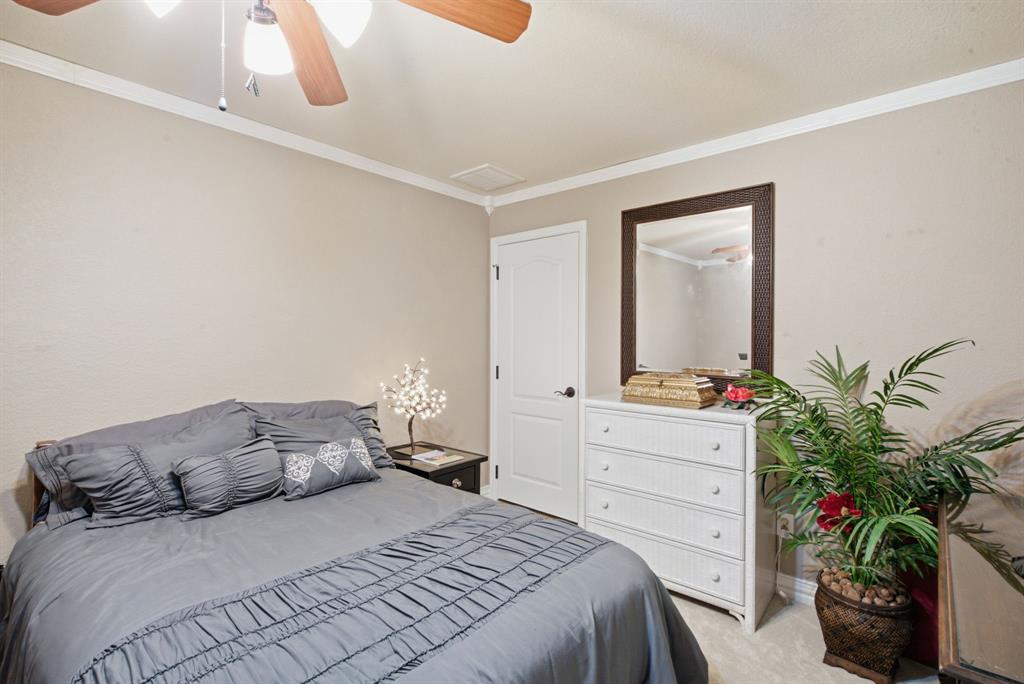 Upstairs bedroom with neutral-toned room featuring a ceiling fan with integrated lighting, crown molding, a paneled interior door, and wall-mounted mirror