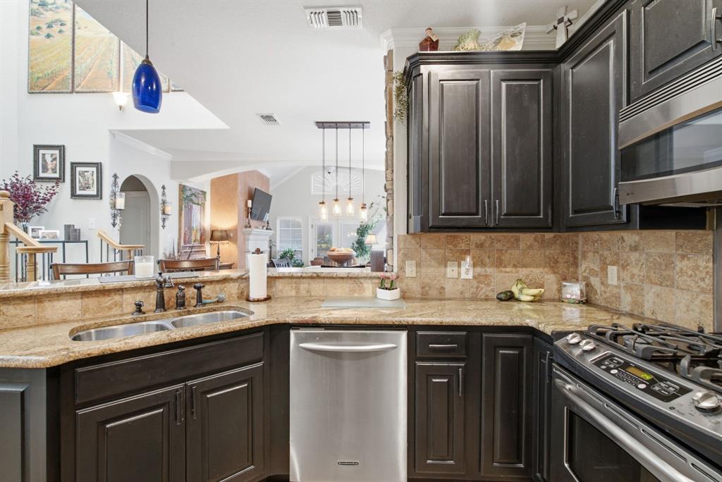 Kitchen featuring dark wood cabinetry, stone countertops, tiled backsplash, dual basin undermount sink, and stainless steel appliances