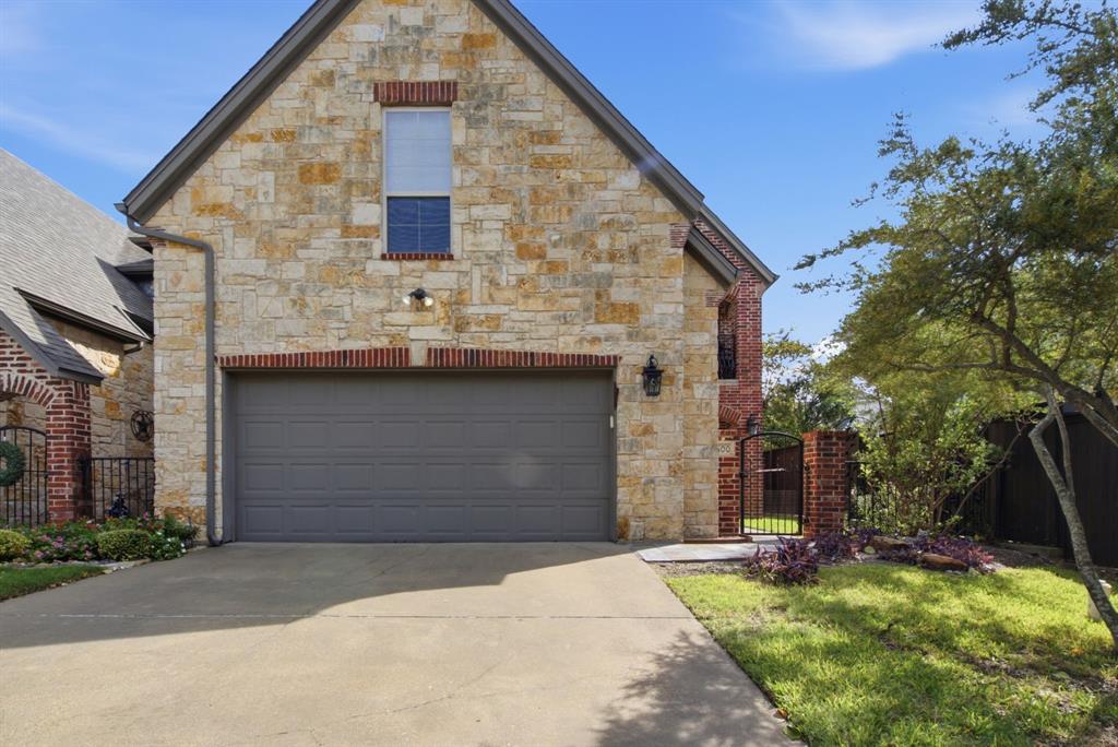 Stone and brick exterior facade featuring a concrete driveway, multi-gabled roofline, metal side-entry gate, and carriage-style outdoor wall lighting