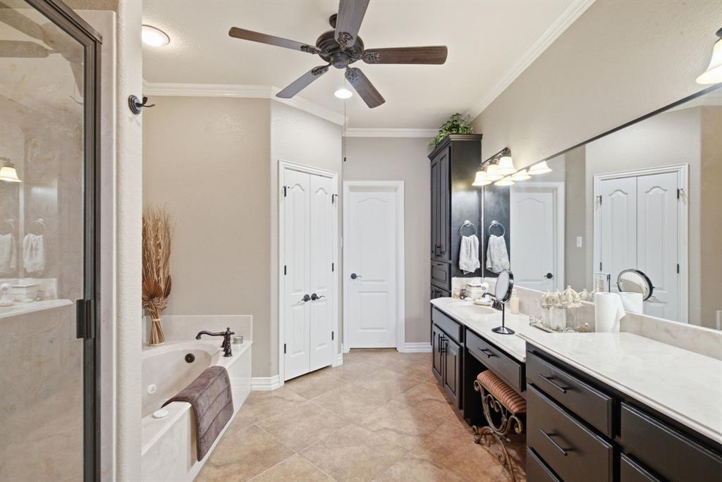 Primary bathroom featuring a dual-sink vanity with dark cabinetry, light-toned countertops, a soaking tub with a wall-mounted faucet, a glass-enclosed shower, and tile flooring