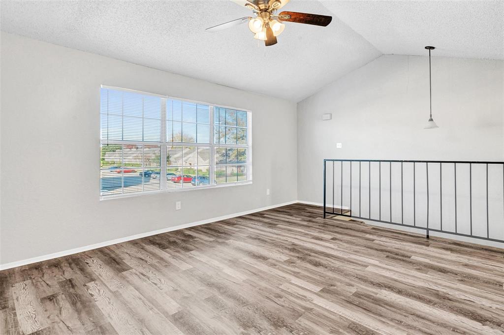 Welcome home to your beautiful spacious living area with vaulted ceilings, ceiling fan, wood-finish flooring, large multi-pane window, and a metal stair railing