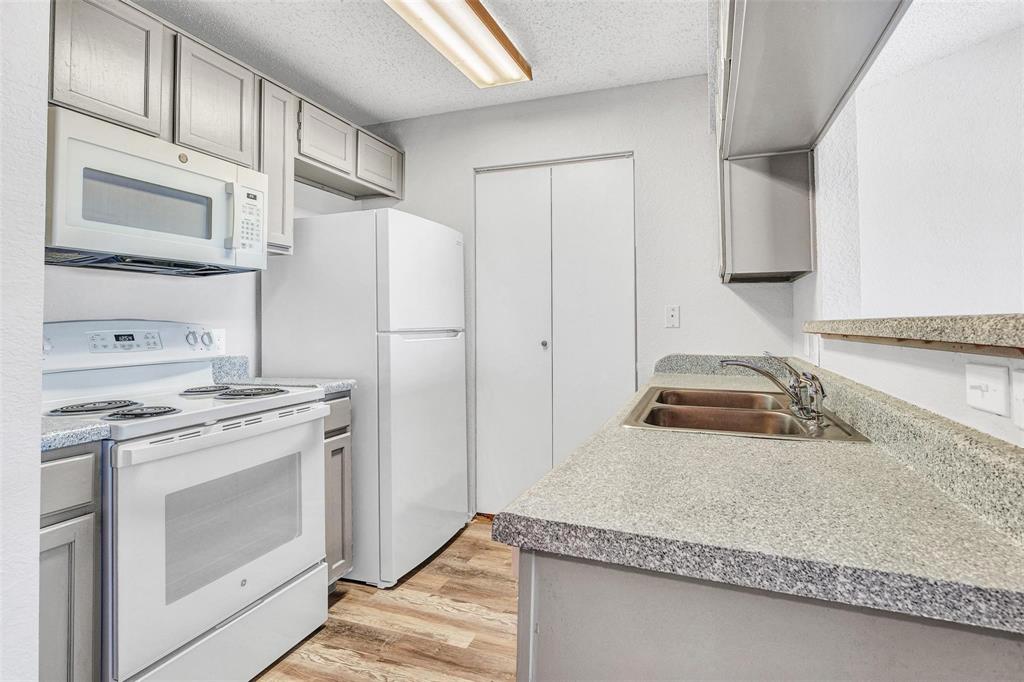 Galley kitchen featuring gray shaker-style cabinetry, white appliances, wood-finish flooring, and a double basin stainless steel sink Galley kitchen featuring gray shaker-style cabinetry, white appliances, wood-finish flooring, and a double basin stainless steel sink
