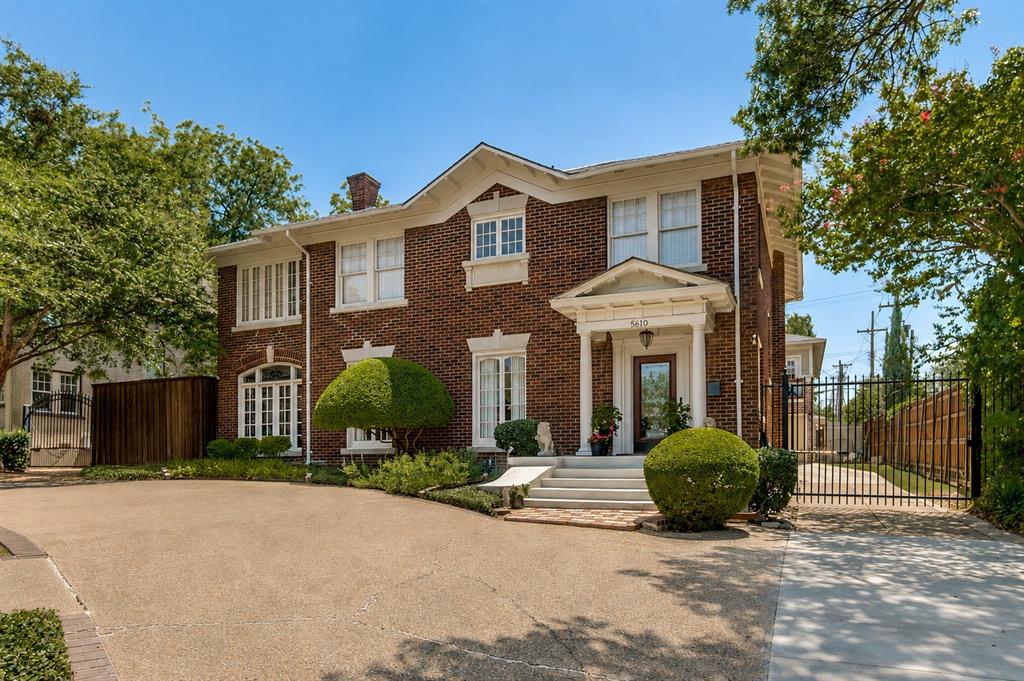 Brick exterior with white trim, columned portico entry, arched windows, manicured shrubbery, and a paved driveway