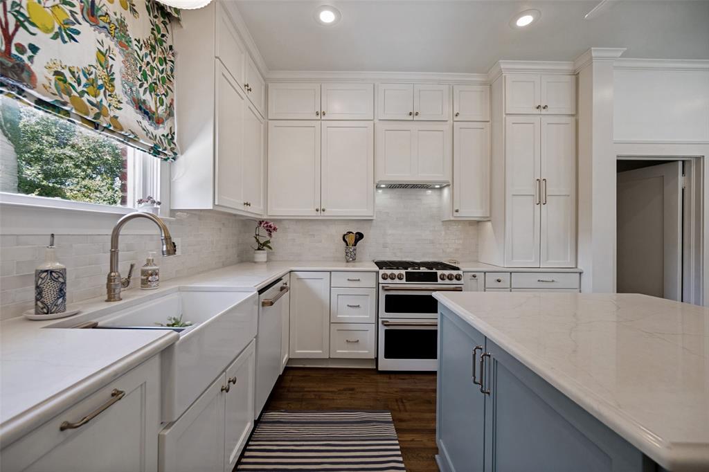 White cabinetry with brushed nickel hardware, expansive countertop space, white subway tile backsplash, farmhouse-style sink, and wood-finish flooring
