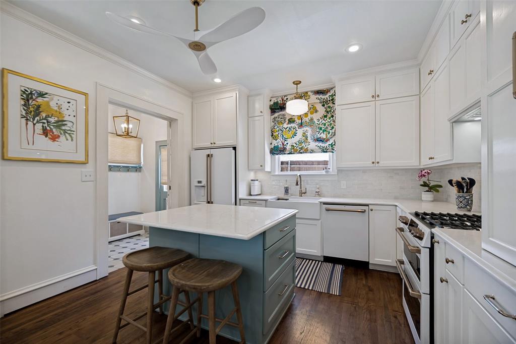 White shaker cabinetry, wood-finish flooring, central island with light countertop, built-in stainless steel appliances, and white subway tile backsplash