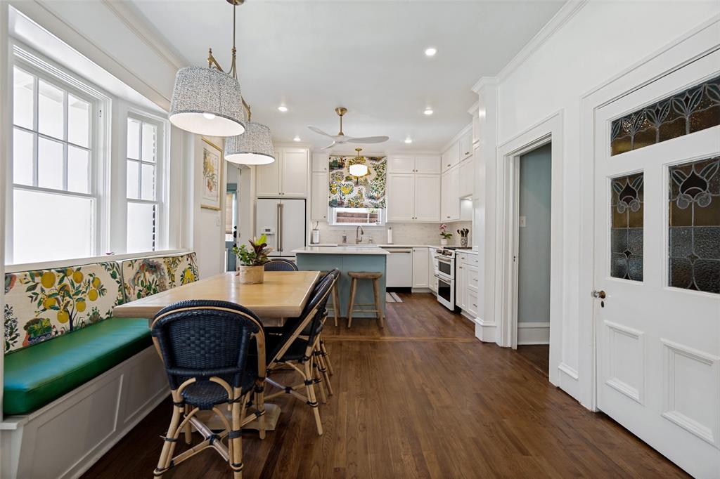 Hardwood flooring, built-in banquette seating with storage, white cabinetry, kitchen island, and stained-glass door