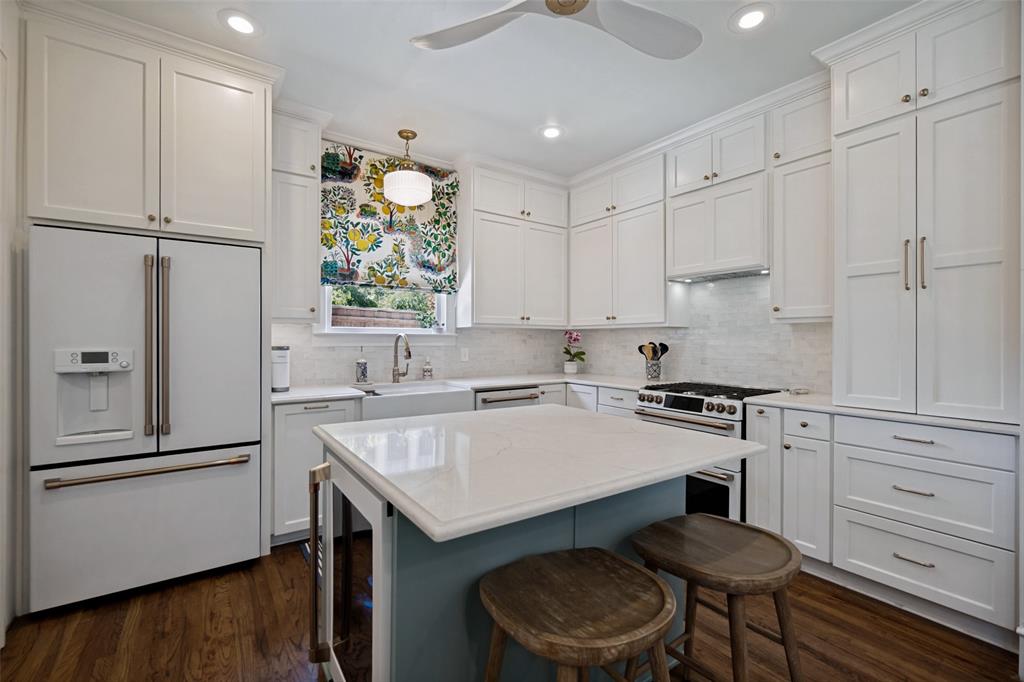 Crisp white cabinetry, wood-finish flooring, central island with seating, stainless steel appliances, and recessed lighting