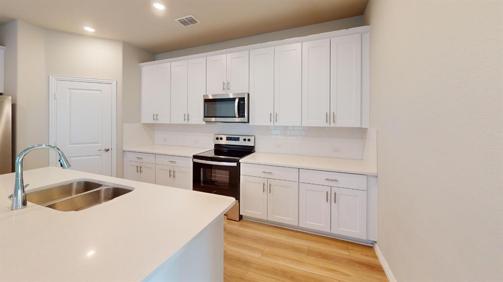 Modern kitchen featuring white shaker cabinetry, stainless steel appliances, a white subway tile backsplash, light-toned countertops, and wood-finish flooring