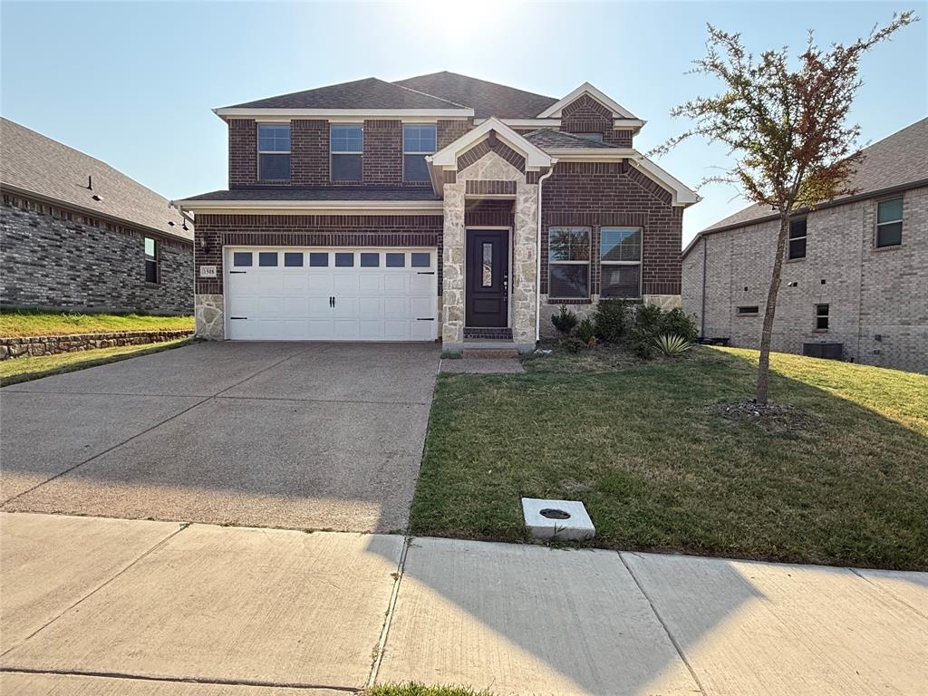 Two-story brick and stone exterior with a two-car garage, concrete driveway, and front entry with a dark-paneled door
