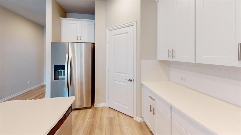 Stainless steel refrigerator with ice and water dispenser, white shaker cabinetry with brushed nickel hardware, light-toned countertops, white subway tile backsplash, and wood-finish flooring