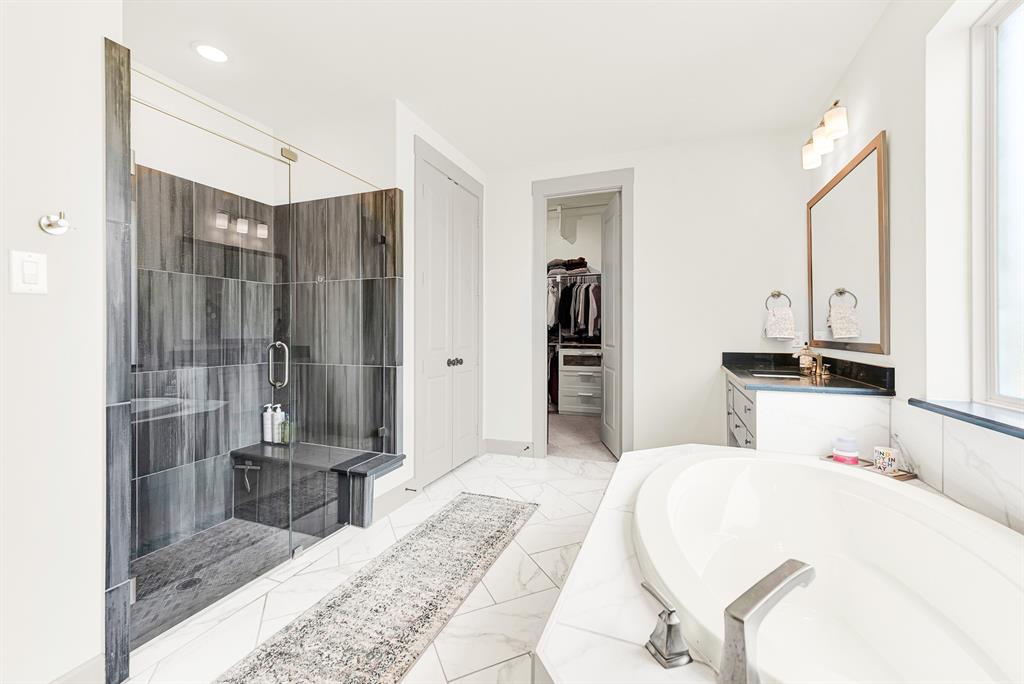 Dark vertical tilework creates bold contrast inside a glass walk-in shower set beside pristine marble counters. Imagine starting brisk morning routines with an invigorating, spa-like shower experience.