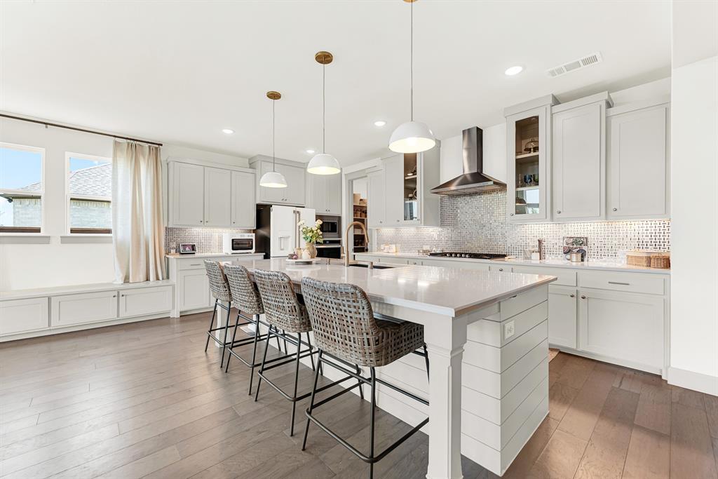 Trio pendant lights illuminate an expansive central prep island anchored by a cozy window bench. Picture lively weekend brunches where everyone gathers for warm pancakes.