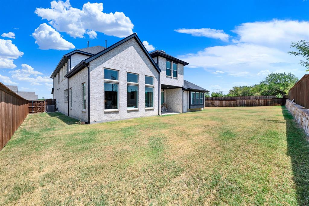 A stacked stone retaining wall aligns with the privacy fence, defining the expansive perimeter under clear skies. Kids and pets can run freely across the sprawling grass during sunny afternoon playtime.