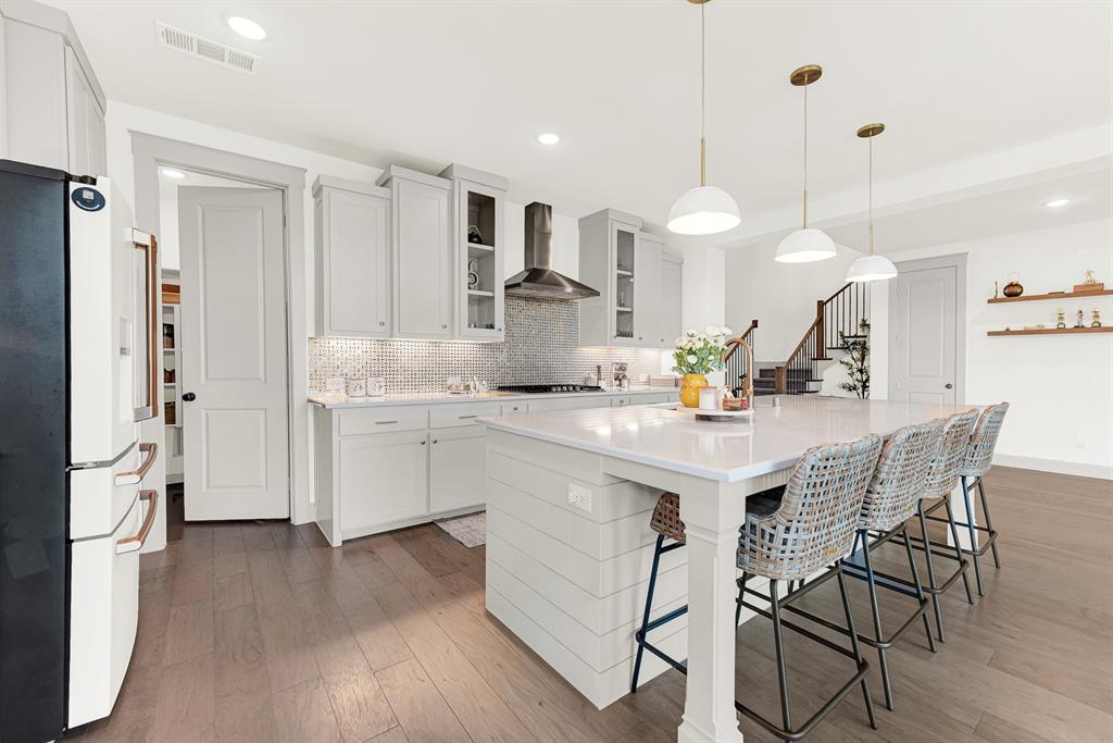 Smooth quartz counters frame a sleek pro-style range hood and walk-in pantry doorway. Imagine grabbing late-night snacks together after a movie in the living room.