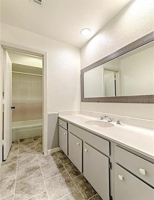 Dual basin vanity with white countertop and cabinetry, tile flooring, and a large mirror with a textured frame