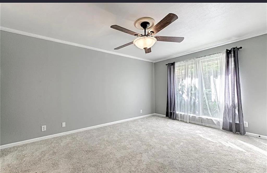 Spacious bedroom with neutral gray walls, soft neutral carpeting, ceiling fan with integrated lighting, and sliding glass doors with sheer and blackout drapery providing natural light control