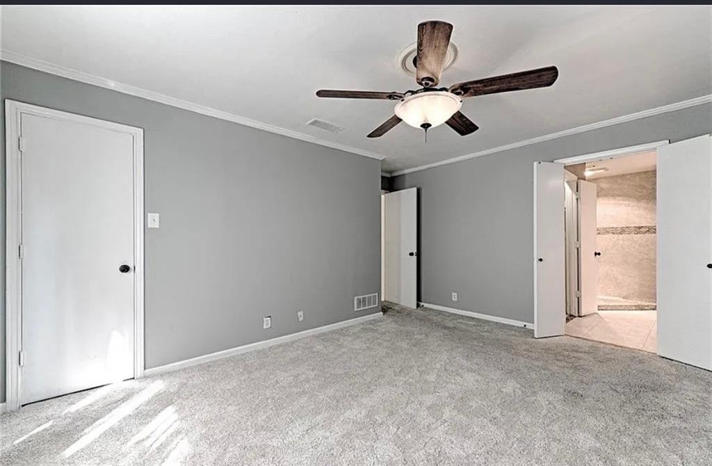Spacious primary bedroom with neutral gray walls, neutral carpet flooring, ceiling fan with integrated lighting, and direct access to an ensuite bathroom