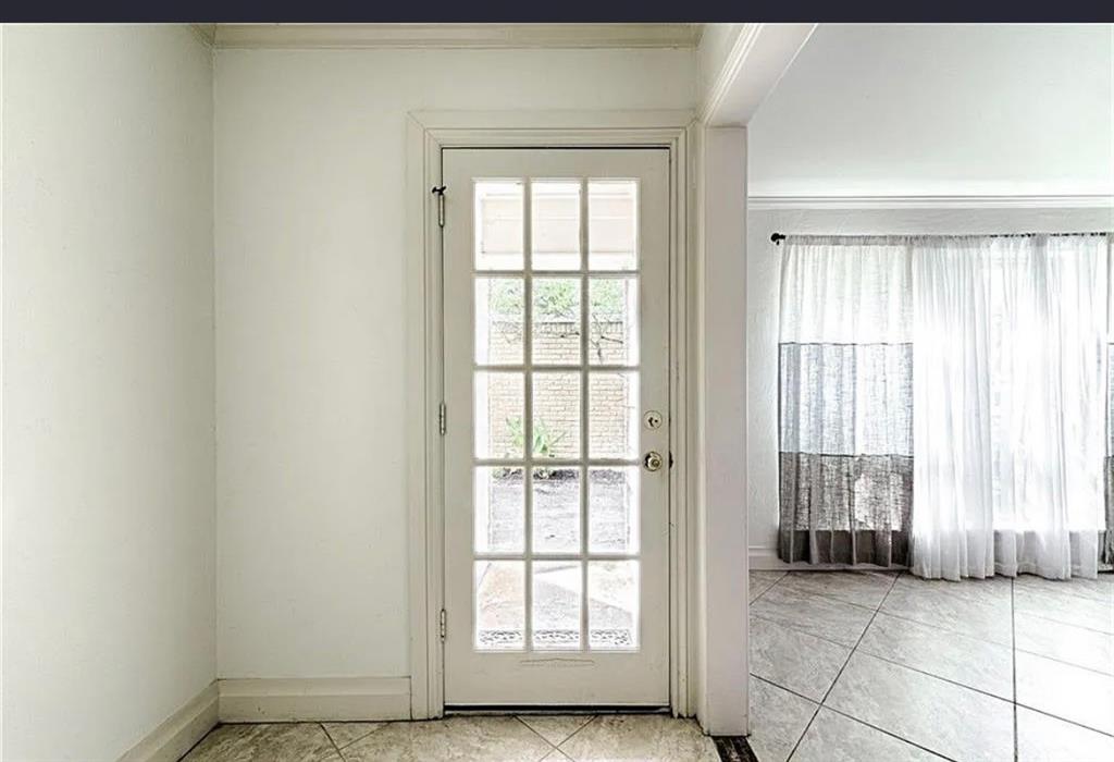 French paneled glass door with white trim, leading to a room featuring large windows with sheer curtains, and large-format tile flooring