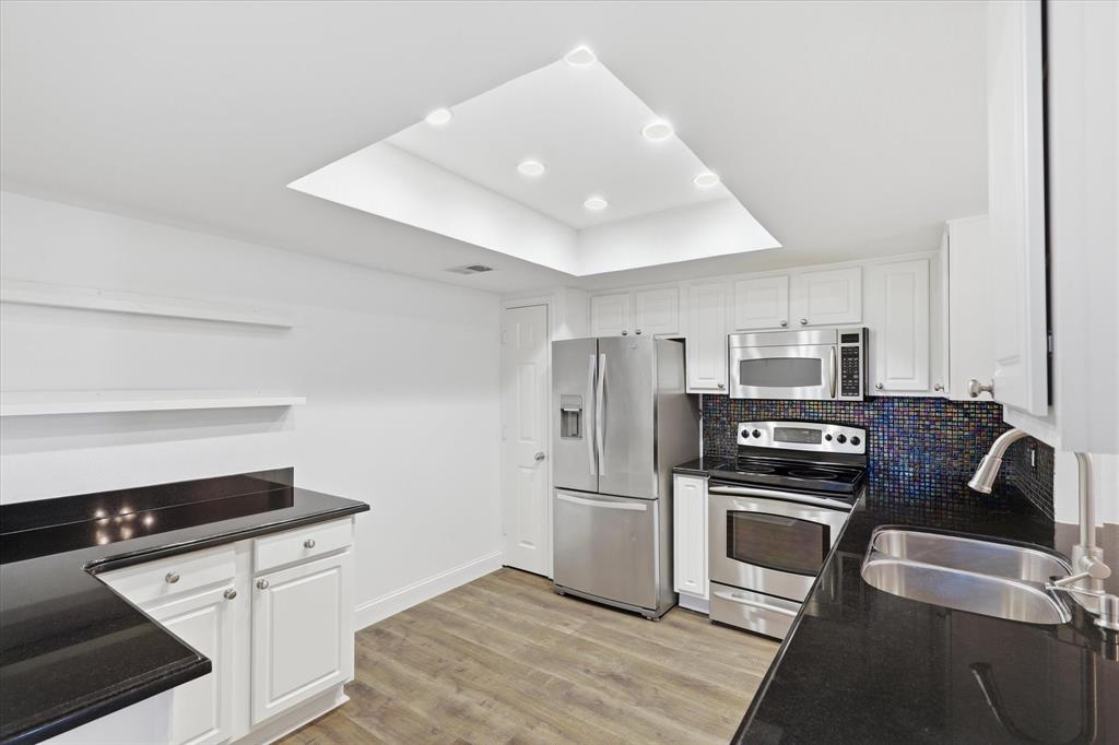 Bright kitchen with white cabinetry, dark countertops, stainless steel appliances and a exit door that brings natural light into the space.