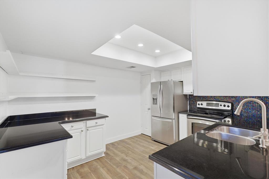 Kitchen view highlighting the white cabinetry, dark countertops, stainless steel appliances and abundant light.