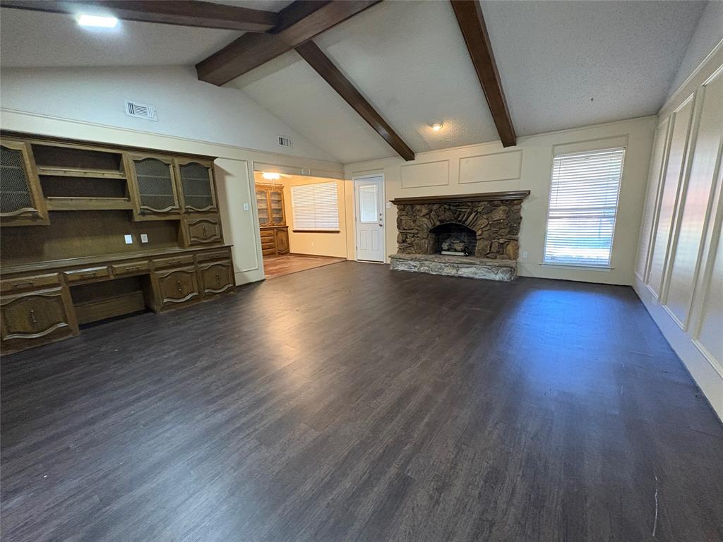 Vaulted ceiling with exposed wood beams, stone fireplace, wood-finish flooring, built-in cabinetry, and panel molding