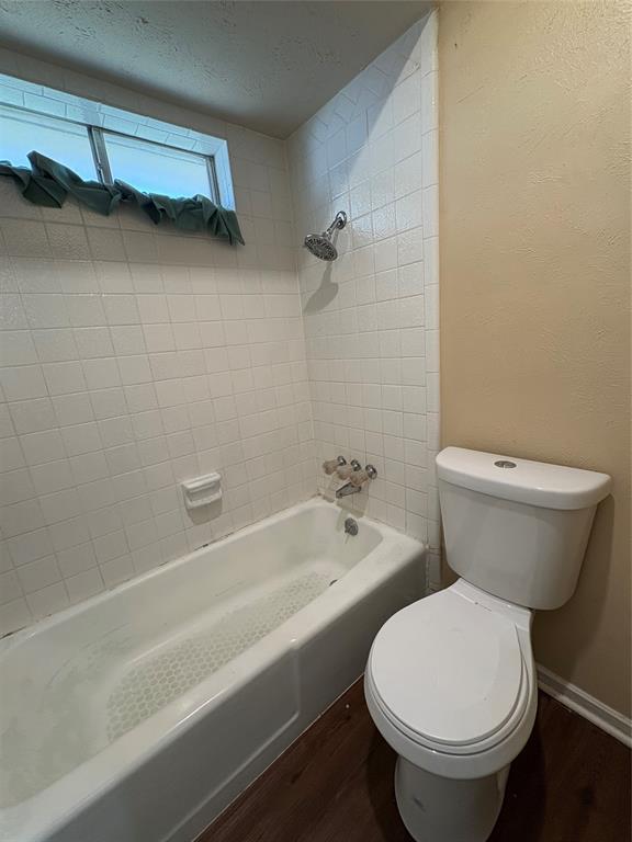 White tiled shower surround, bathtub, toilet, and wood-finish flooring