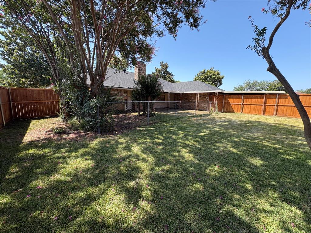 Expansive backyard featuring a manicured lawn, wood fencing, covered patio, and mature trees