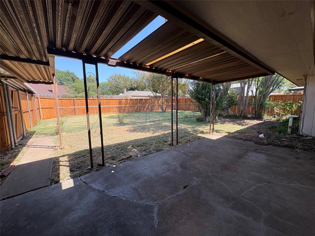 Covered patio with concrete flooring, framed by a wood fence, leading to a grass area