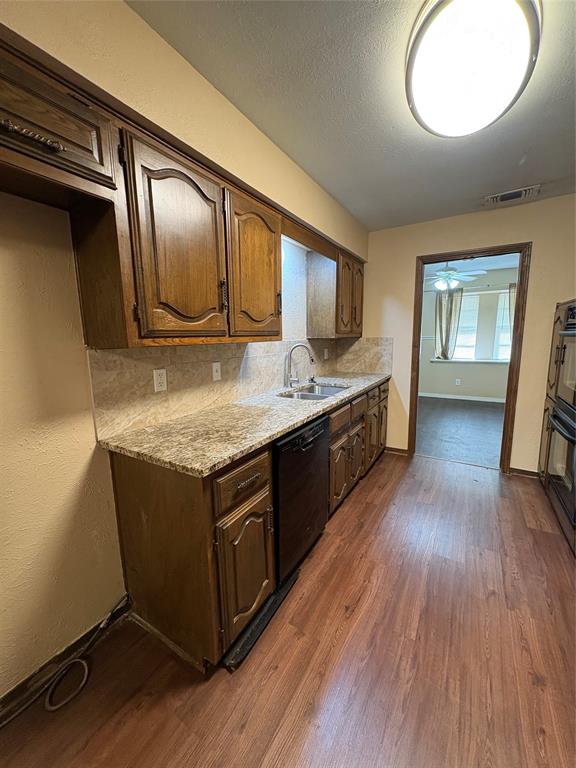 Kitchen featuring wood-finish flooring, wood cabinetry, stone-finish countertops, a stainless steel sink with a gooseneck faucet, and a built-in dishwasher