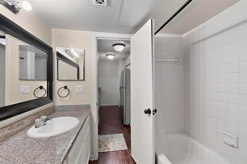 Bathroom featuring a vanity with an integrated sink, a dark framed mirror, and a tiled shower with a built-in tub