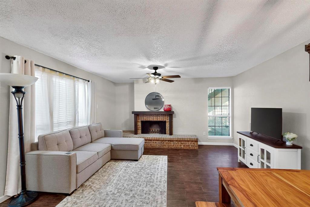 Living area featuring wood-finish flooring, a brick fireplace with a wood mantle, and a ceiling fan