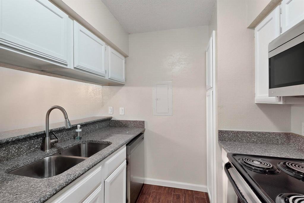 White upper and lower cabinetry, dual basin stainless steel sink with gooseneck faucet, dark speckled countertops, wood-finish flooring, and a stainless steel over-the-range microwave