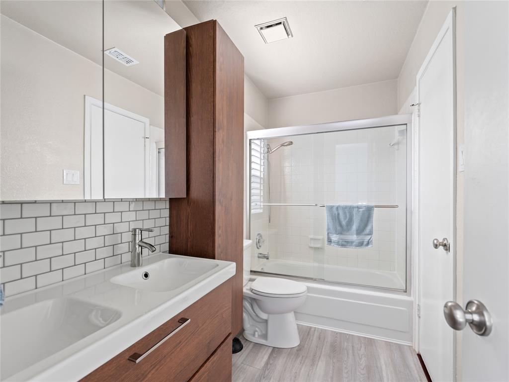 Vanity with integrated dual sinks, subway tile backsplash, wood-finish cabinetry, and a shower-tub combination with sliding glass doors