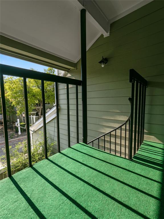 Balcony featuring green outdoor carpeting, black metal railings, and a wall-mounted light fixture