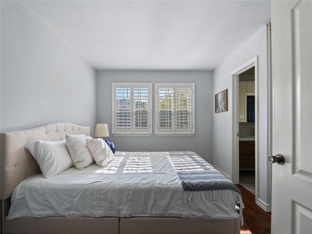 Two windows with white plantation shutters, an upholstered tufted headboard, and wood-finish flooring Two windows with white plantation shutters, an upholstered tufted headboard, and wood-finish flooring