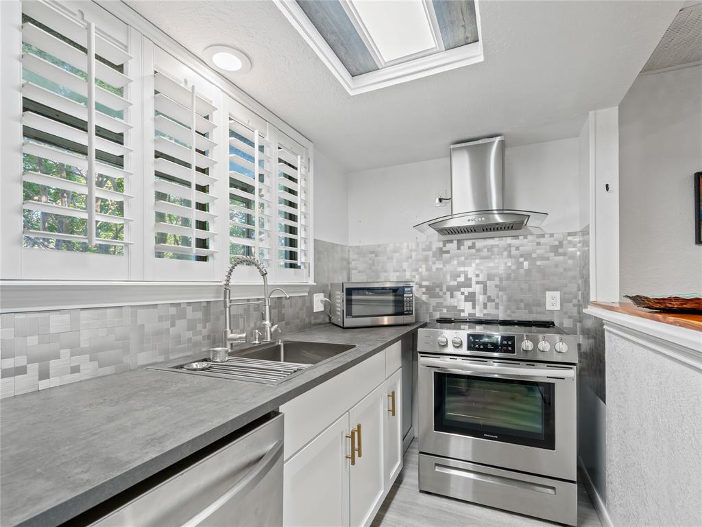 Kitchen featuring stainless steel appliances, solid surface countertops, a mosaic tile backsplash, a skylight, and white plantation shutters Kitchen featuring stainless steel appliances, solid surface countertops, a mosaic tile backsplash, a skylight, and white plantation shutters