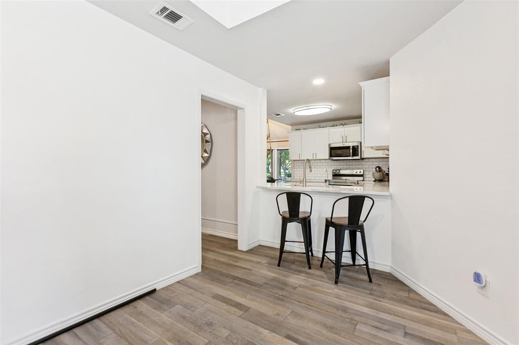 Wood-finish flooring throughout, white baseboards, and a kitchen featuring white cabinetry, a subway tile backsplash, and stainless steel appliances