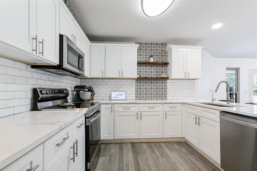 White cabinetry with brushed nickel hardware, light-toned countertops, subway tile backsplash, patterned accent tile, and wood-finish flooring White cabinetry with brushed nickel hardware, light-toned countertops, subway tile backsplash, patterned accent tile, and wood-finish flooring