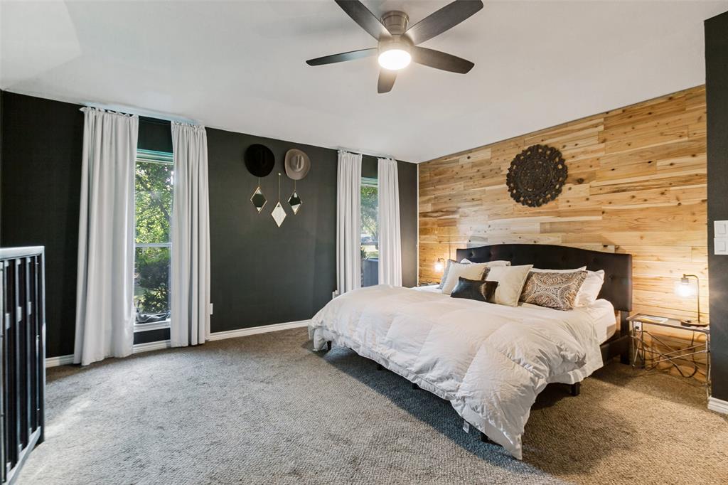 Primary Bedroom Suite with Accent Wood-Finish Wall Paneling, Ceiling Fan with Integrated Lighting, Black Metal Bed Frame, Dual Glass Doors Opening to Natural Light, and Plush Carpeting Throughout Primary Bedroom Suite with Accent Wood-Finish Wall Paneling, Ceiling Fan with Integrated Lighting, Black Metal Bed Frame, Dual Glass Doors Opening to Natural Light, and Plush Carpeting Throughout