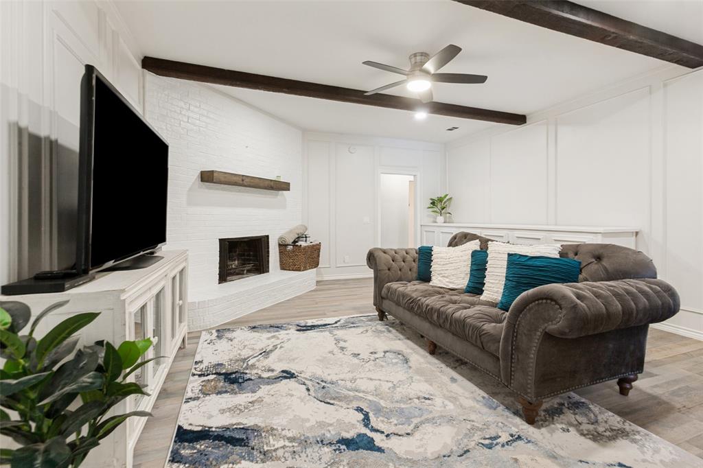 White brick fireplace with a wood mantel, wood-finish flooring, and exposed ceiling beams White brick fireplace with a wood mantel, wood-finish flooring, and exposed ceiling beams