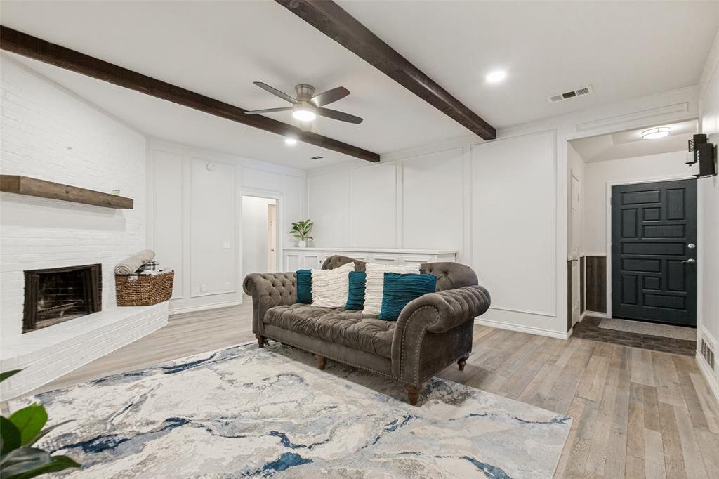 Living area featuring a white brick fireplace, wood-finish flooring, exposed ceiling beams, recessed lighting, and a detailed entry door Living area featuring a white brick fireplace, wood-finish flooring, exposed ceiling beams, recessed lighting, and a detailed entry door