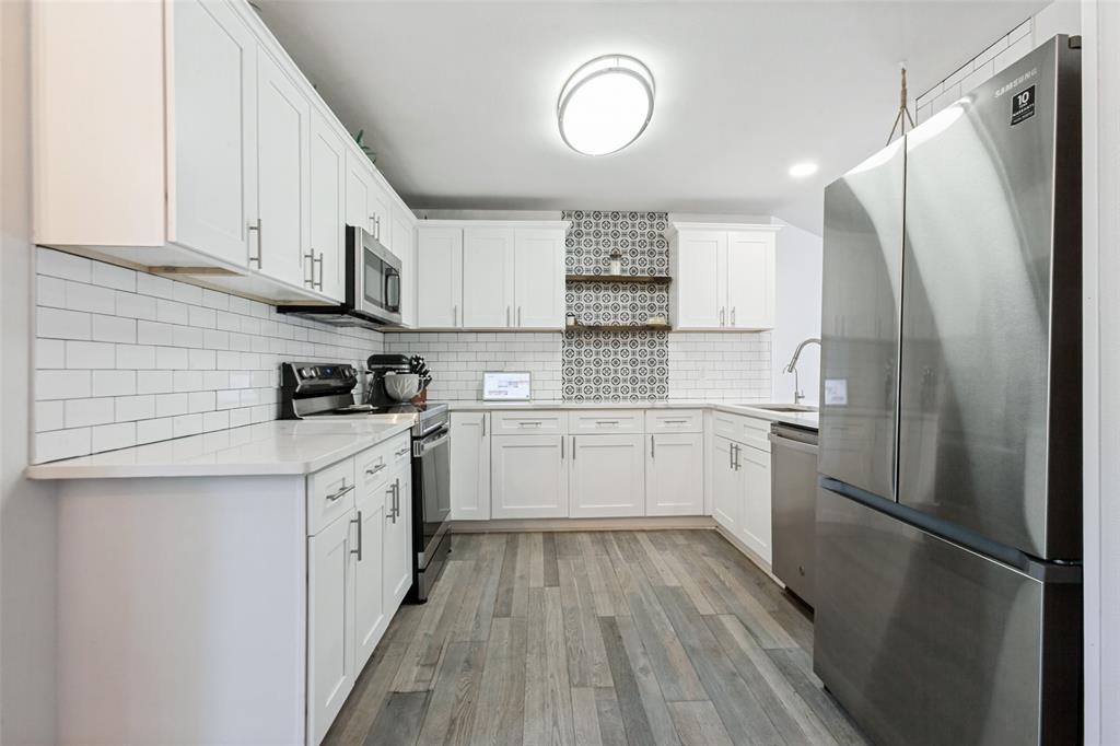 White cabinetry with stainless steel appliances, white subway tile backsplash, patterned accent tile, and wood-finish flooring