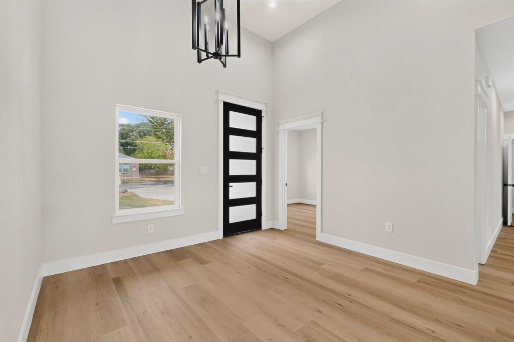 Vaulted ceiling with a black geometric chandelier, wood-finish flooring, white walls, and a black paneled door