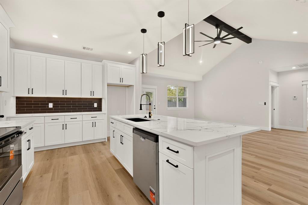Kitchen featuring white shaker cabinetry, an island with a light-toned countertop, wood-finish flooring, a dark subway tile backsplash, and vaulted ceilings