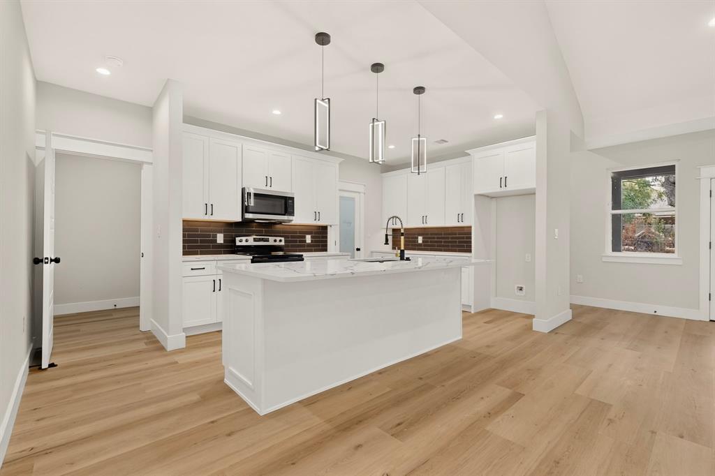 Open-concept kitchen with white cabinetry, a central island with a stone-finish countertop, and wood-finish flooring