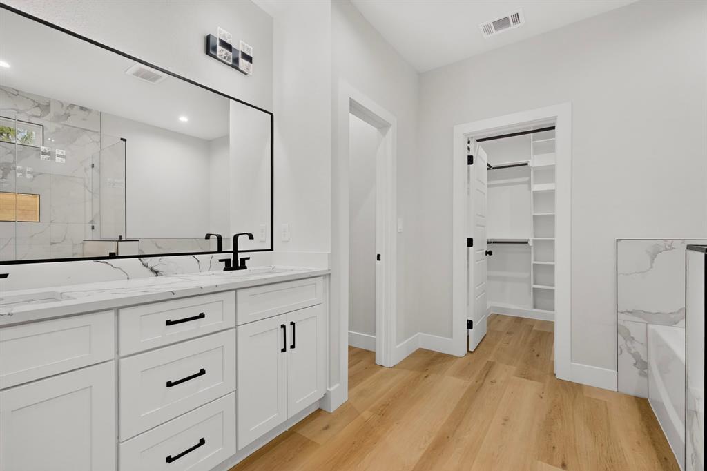 Dual vanity with white cabinetry and black hardware, stone-finish countertop, wood-finish flooring, and walk-in closet with shelving