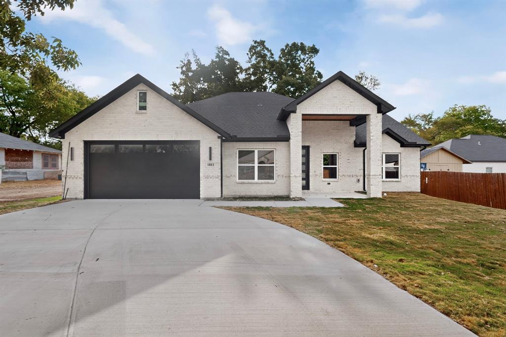 Modern exterior featuring light-colored brick, a dark roof, a two-car garage with frosted panels, and a covered entry